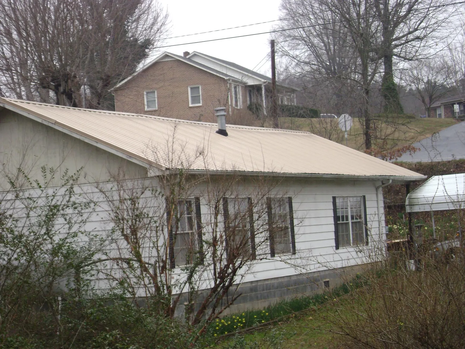 Tan metal roof on a white sided house set into a hillside — Commercial Roofing by Roofing Brothers in Byron