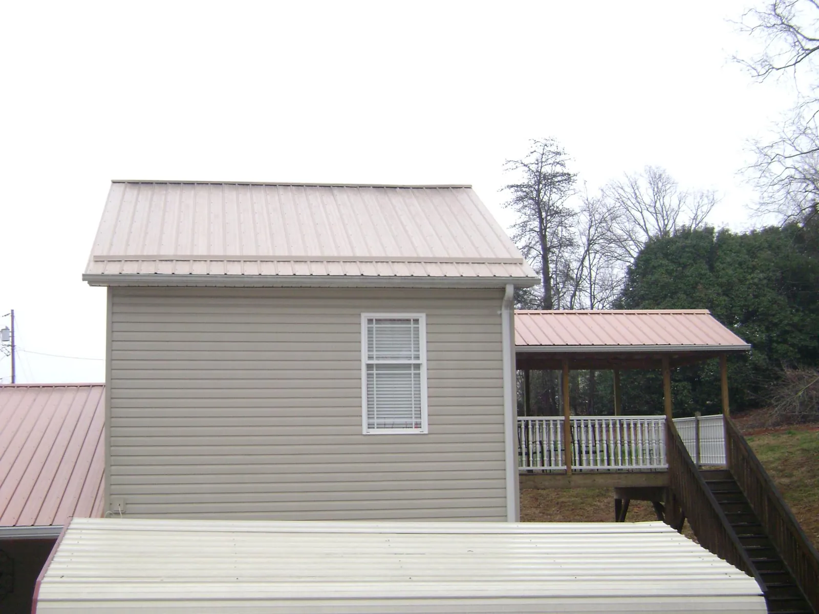 Tan metal roofs on a two story addition and attached porch, from a Roof Replacement job in Byron